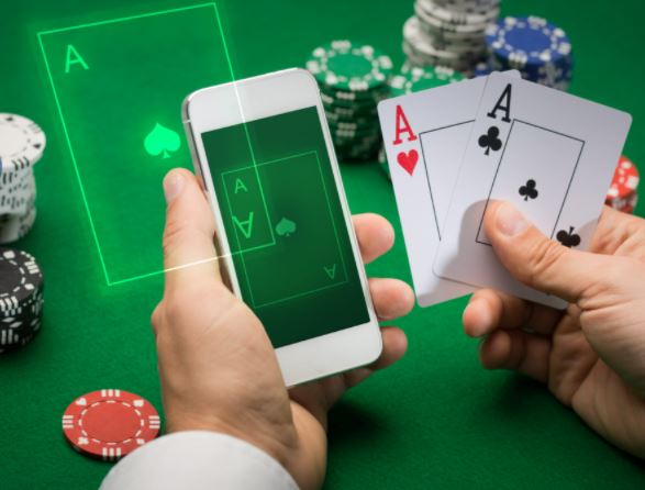 Två händer som håller i en mobiltelefon och två spelkort på ett spelbord fullt av spelmarker.